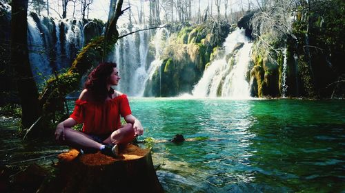 Woman sitting on rock looking at waterfall in forest
