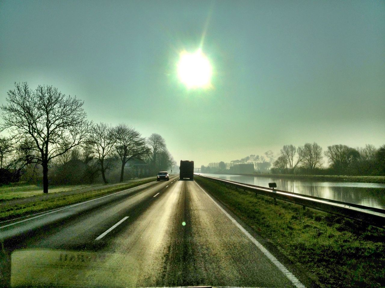 transportation, tree, sun, road, the way forward, sky, water, grass, sunlight, diminishing perspective, vanishing point, car, nature, tranquility, lens flare, sunbeam, bare tree, tranquil scene, reflection, no people