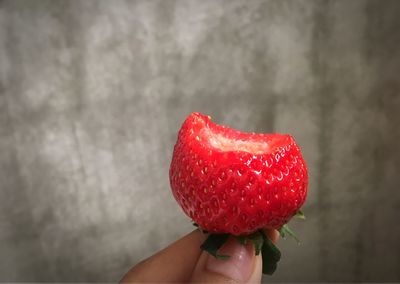 Cropped hand holding strawberry against wall