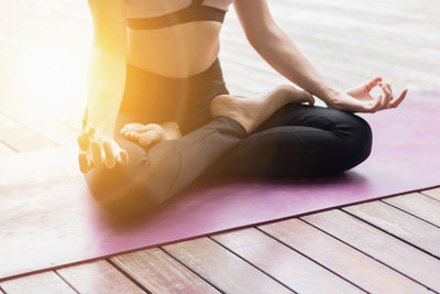 Low section of young woman exercising on floorboard against sky during sunset