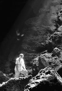 Man standing on rock formation in cave during sunny day