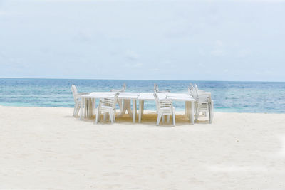 Empty chairs on beach against sky