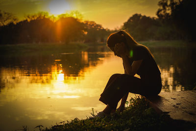 Side view of silhouette woman looking at lake during sunset