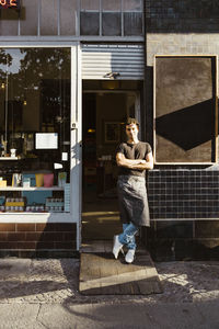 Male owner with arms crossed standing outside cafe on sunny day