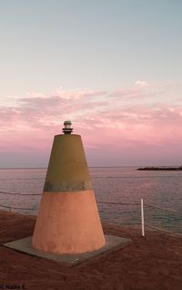 Lighthouse by sea against sky during sunset