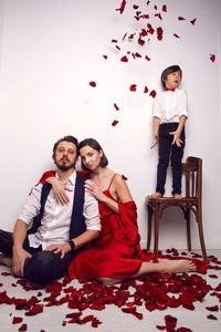 Couple sitting on the floor in an apartment on valentine's day. boy son cupid throws red rose petals