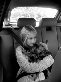 Thoughtful girl holding dog while traveling in car