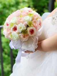 Midsection of bride holding bouquet outdoors