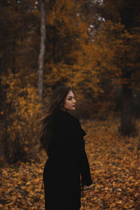 Rear view of beautiful young woman standing in forest during autumn