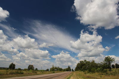 Road passing through field against cloudy sky