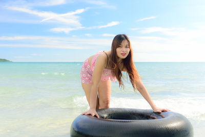 Portrait of beautiful woman leaning on inflatable ring in sea against sky