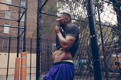 Basketball player wiping sweat while leaning on chainlink fence