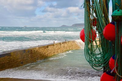 Buoys hanging at beach against cloudy sky