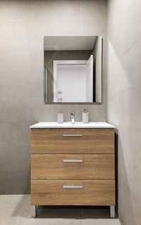 Modern refurbished bathroom in minimalist style with gray tiled walls, mirror and wooden drawers 