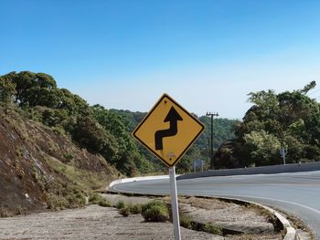 Road sign by trees against clear blue sky