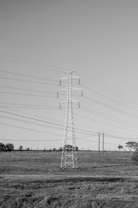 Electricity pylons on field against clear sky