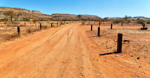 Wooden posts on dirt road amidst field against clear sky
