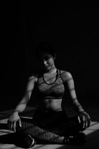 Full length of young woman relaxing while sitting on floor in darkroom at home