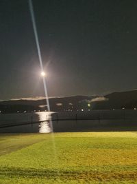 Illuminated street light on field against sky at night