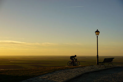 Silhouette of man riding bicycle on road during sunset