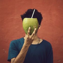 Close-up of man holding fruit against orange wall