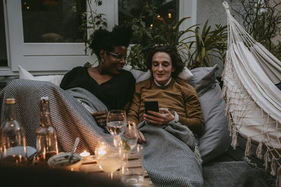 Smiling man using smart phone by friend in yard during social gathering