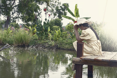 A depressed woman sits alone at the edge of a lake, thinking for a short time.