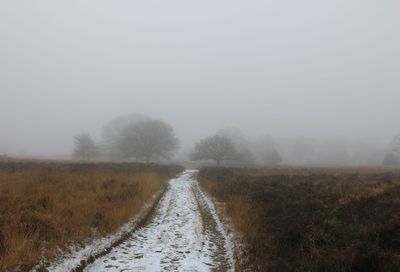 Dirt road amidst field against sky during winter