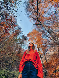 Portrait of young woman standing by trees during autumn