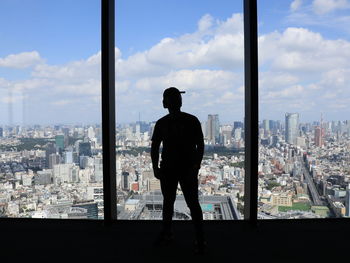 Rear view of man looking at cityscape against sky