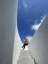 Low angle view of woman climbing on wall against sky