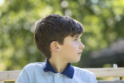 Close up portrait front view of serious young boy looking away sitting on a bench. bokeh background.