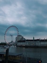 Ferris wheel in city against cloudy sky