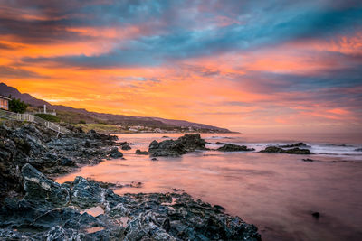 Rocky seashore against cloudy sky during sunset