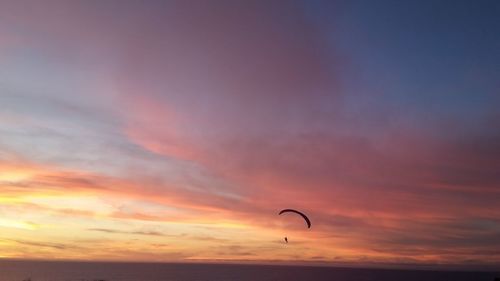 Person paragliding over sea against sky during sunset