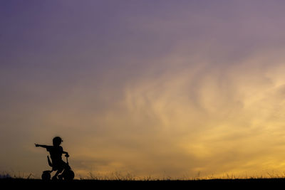 Silhouette girl riding bicycle against sky during sunset
