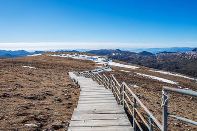 Footpath leading towards mountains against clear blue sky