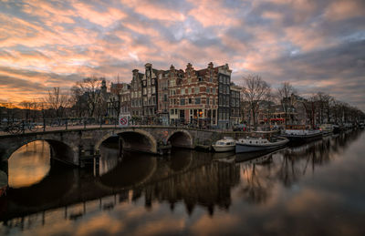 Bridge over river in city against sky during sunset