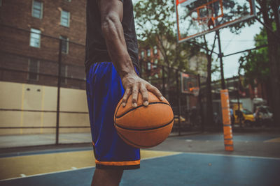 Midsection of young man holding basketball at court