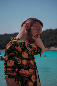 Thoughtful man standing at beach against clear sky