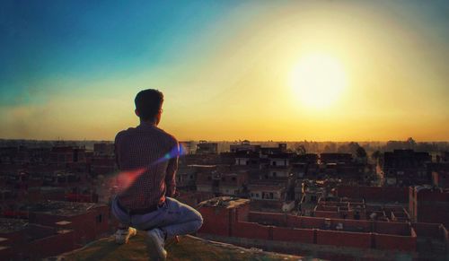 Rear view of man looking at city against sky during sunset