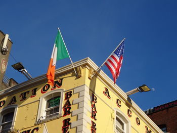 Low angle view of irish and american flags on building against clear blue sky