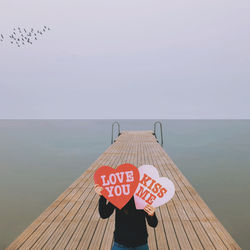 High angle view of woman holing heart shape with text while standing on pier