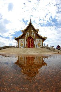 Buddhist temple reflecting on puddle against cloudy sky