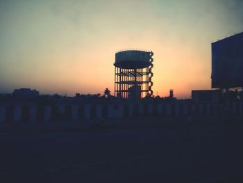 Water tower in factory against sky during sunset