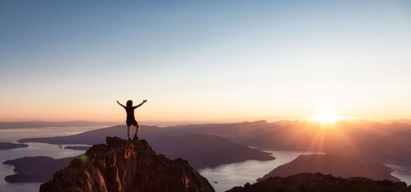 Silhouette person standing on rock against sky during sunset