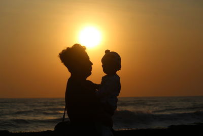 Silhouette woman standing at beach against sky during sunset