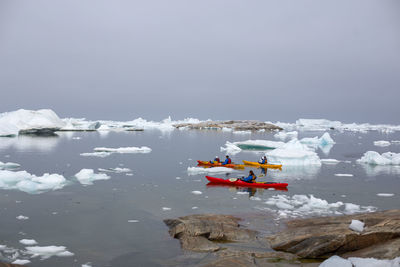 People floating on lake against sky during winter