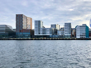 Modern buildings by river against sky in city