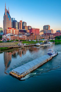 Sailboats in river by buildings against clear sky